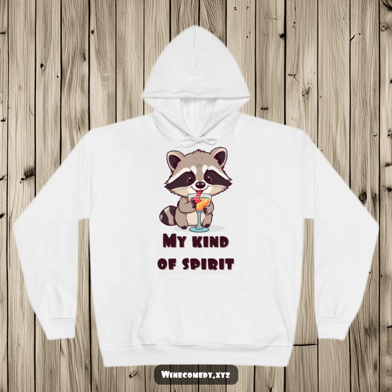 Funny raccoon artistically swirling wine in a tiny glass, featured on a warm, cozy hoodie, perfect for winter fun.
